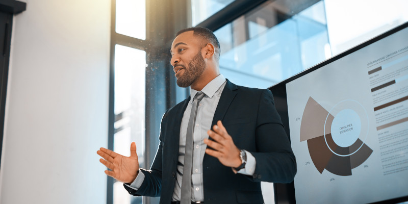 Man is standing in front of a tv screen and presenting business data