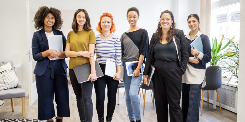 A group of colleagues stand in an office setting, facing the camera.