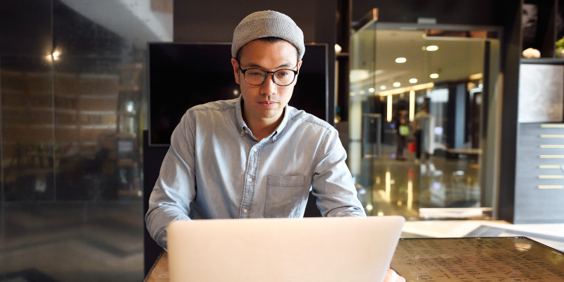 Image shows a man seated at a desk working on a laptop.